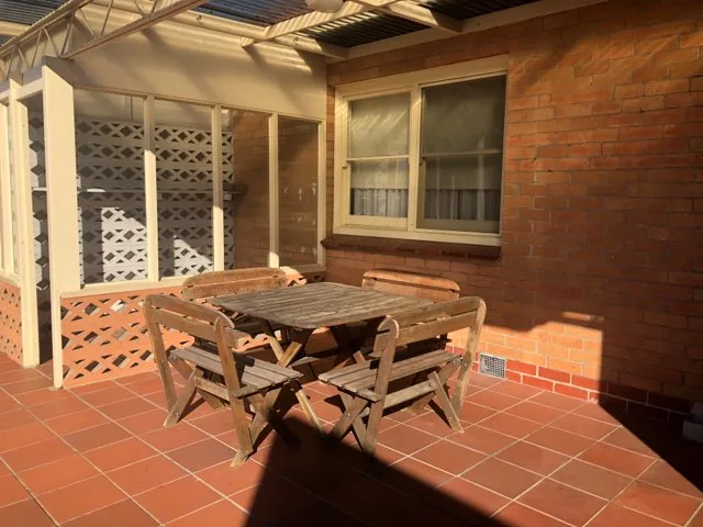 A timber table and chairs sit on the tiled patio beside a brick wall.