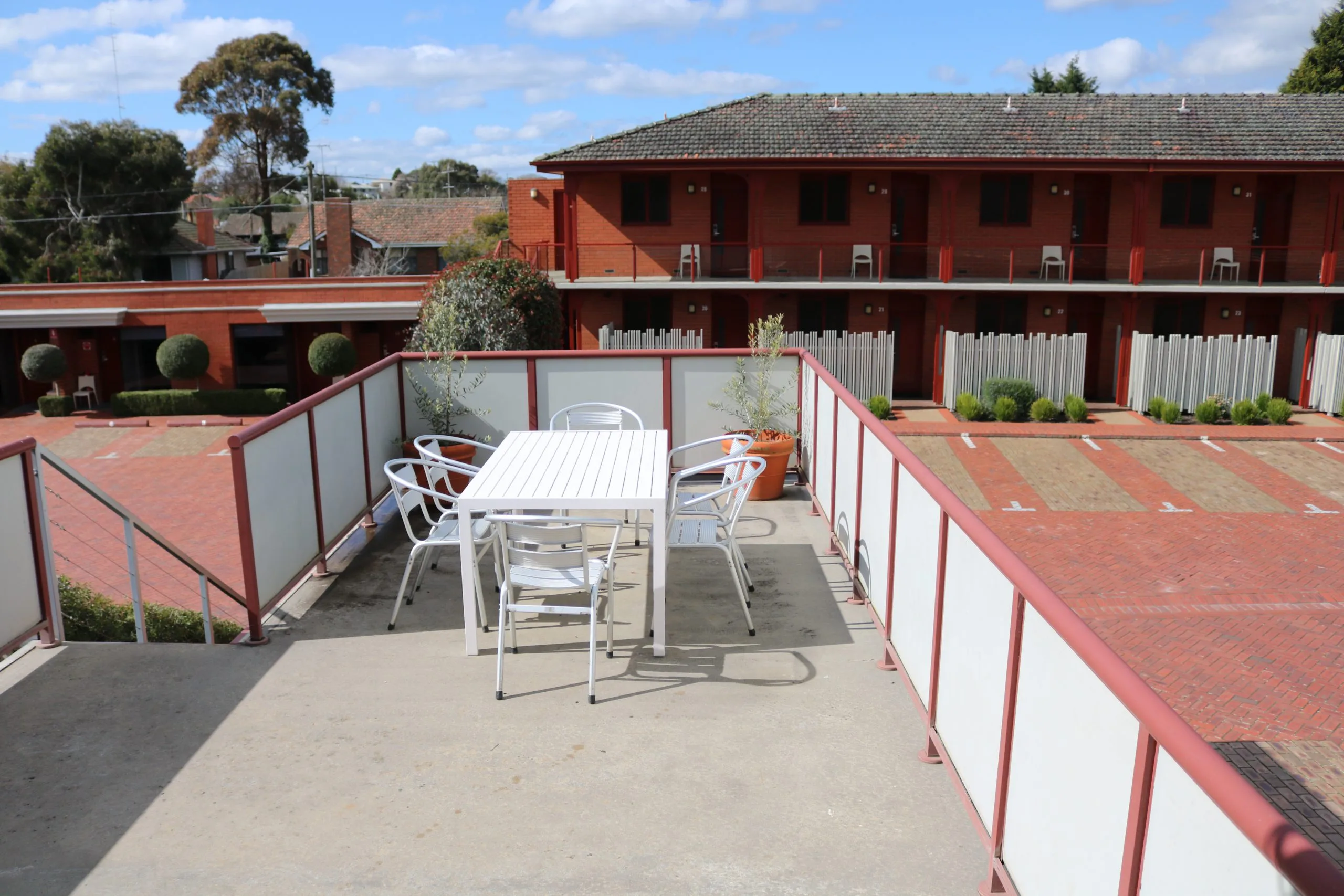 A white outdoor table and chairs sit on an apartment patio overlooking a brick motel courtyard.