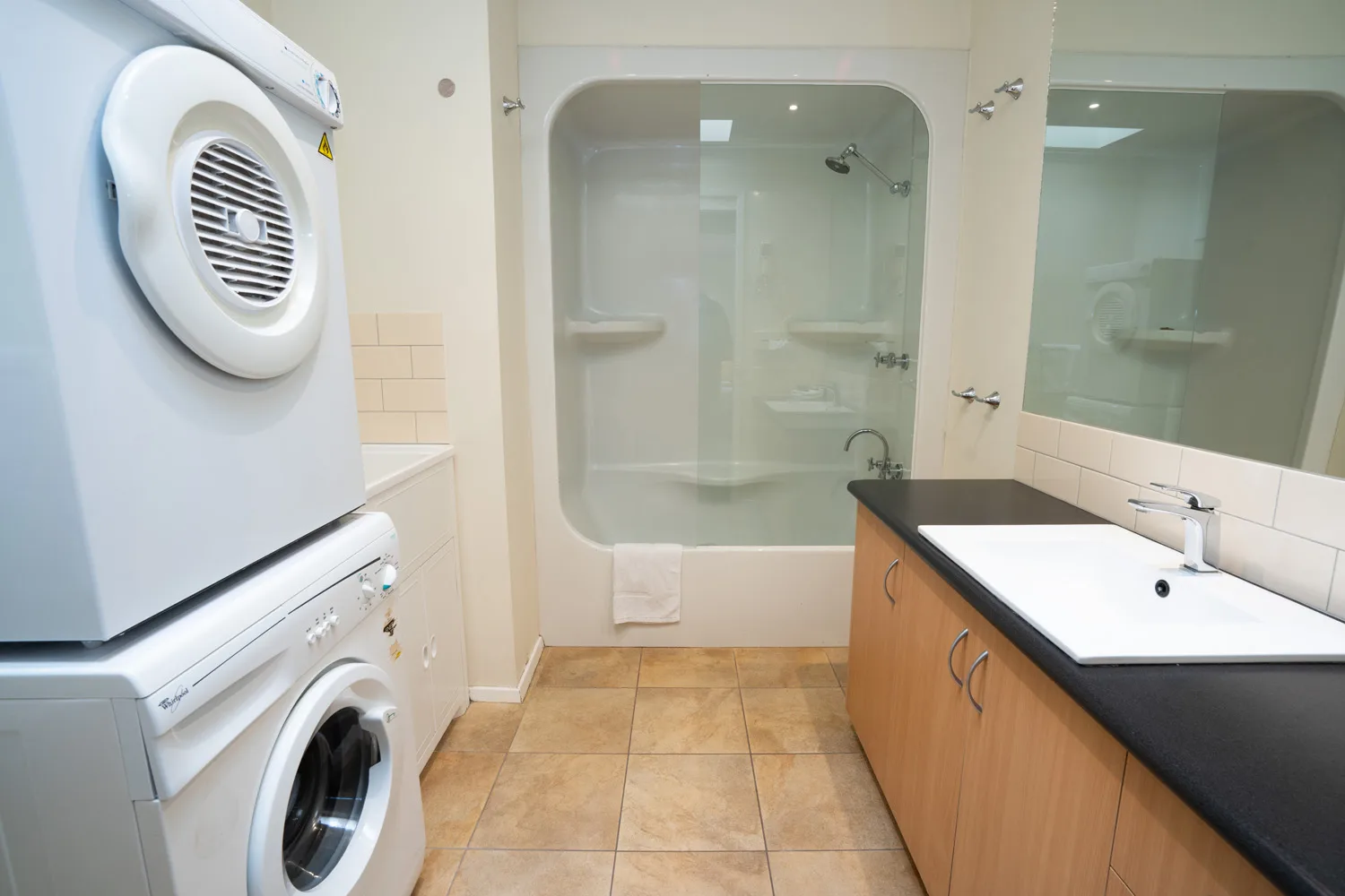 Apartment bathroom with a stacked washer and dryer, bathtub and vanity.