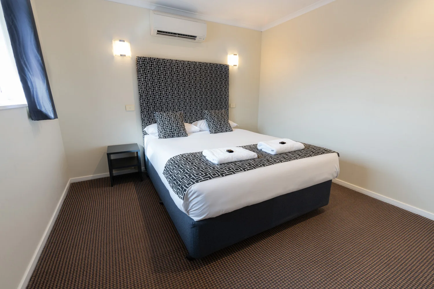 A neatly made bed with black-and-white geometric bedding in a motel bedroom.