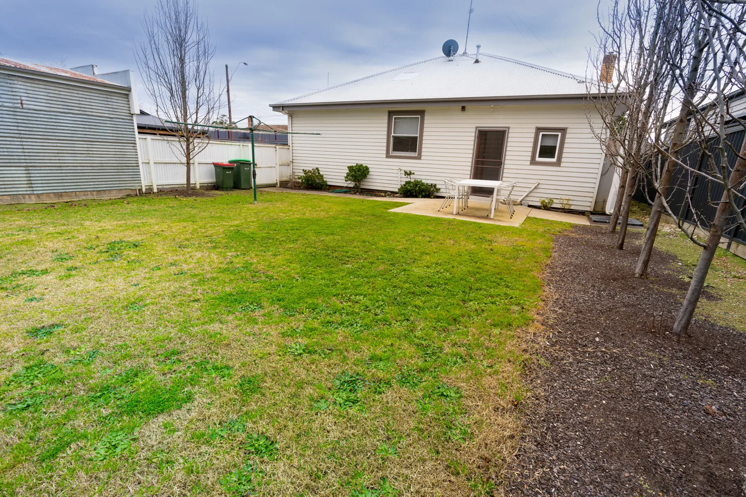 A grassy backyard with a patio table beside a single-storey house.