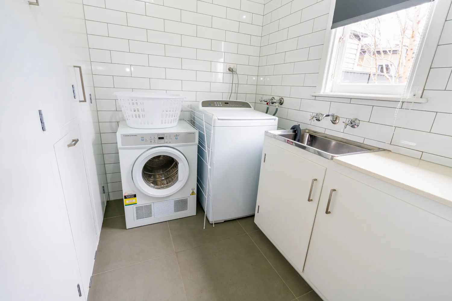 A laundry room with a front-loading dryer, washing machine and stainless-steel sink.
