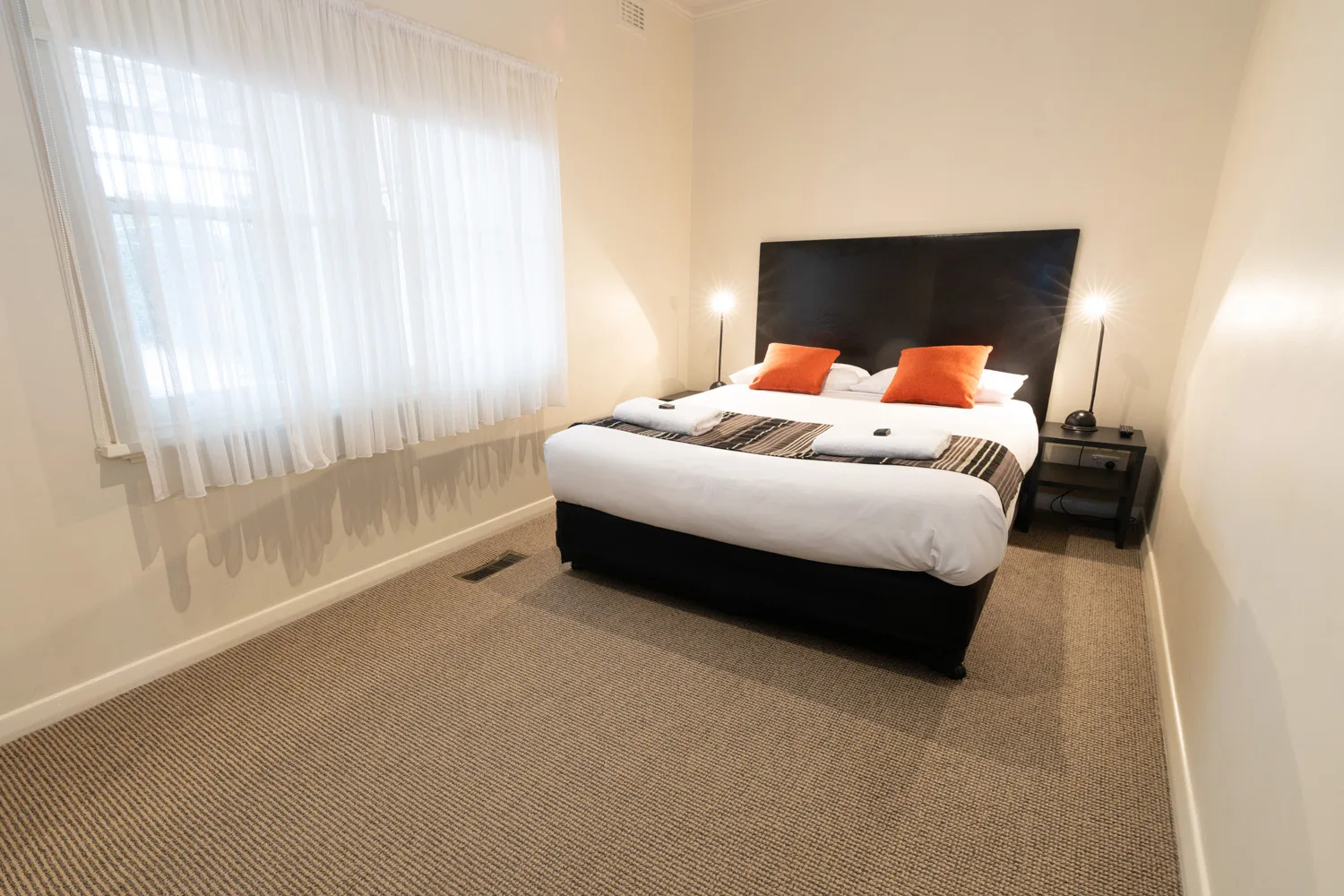 A white bed with orange cushions sits between two bedside lamps.