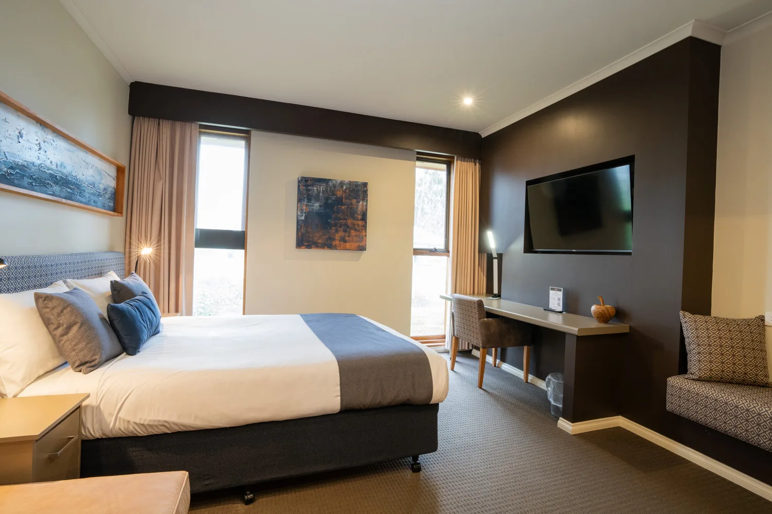 A motel bedroom with a neatly made bed, desk and wall-mounted television.