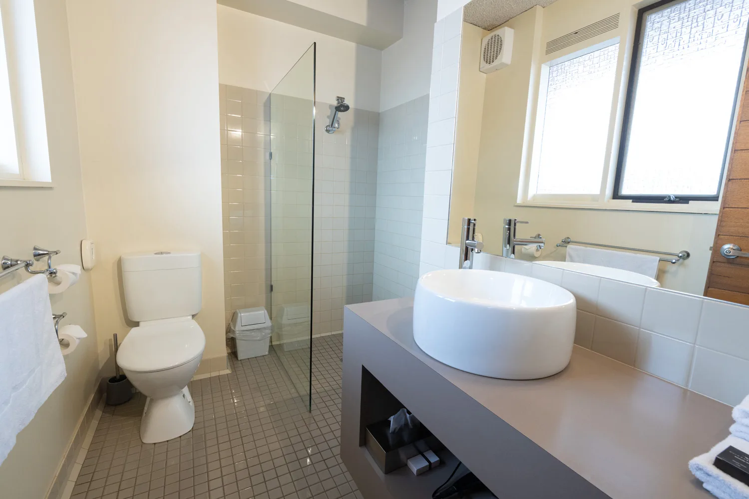 Guest room bathroom with a glass shower, toilet and round vessel basin.