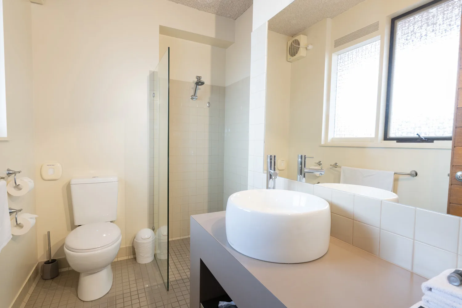 A guest bathroom with a glass-enclosed shower, toilet and round vessel basin.