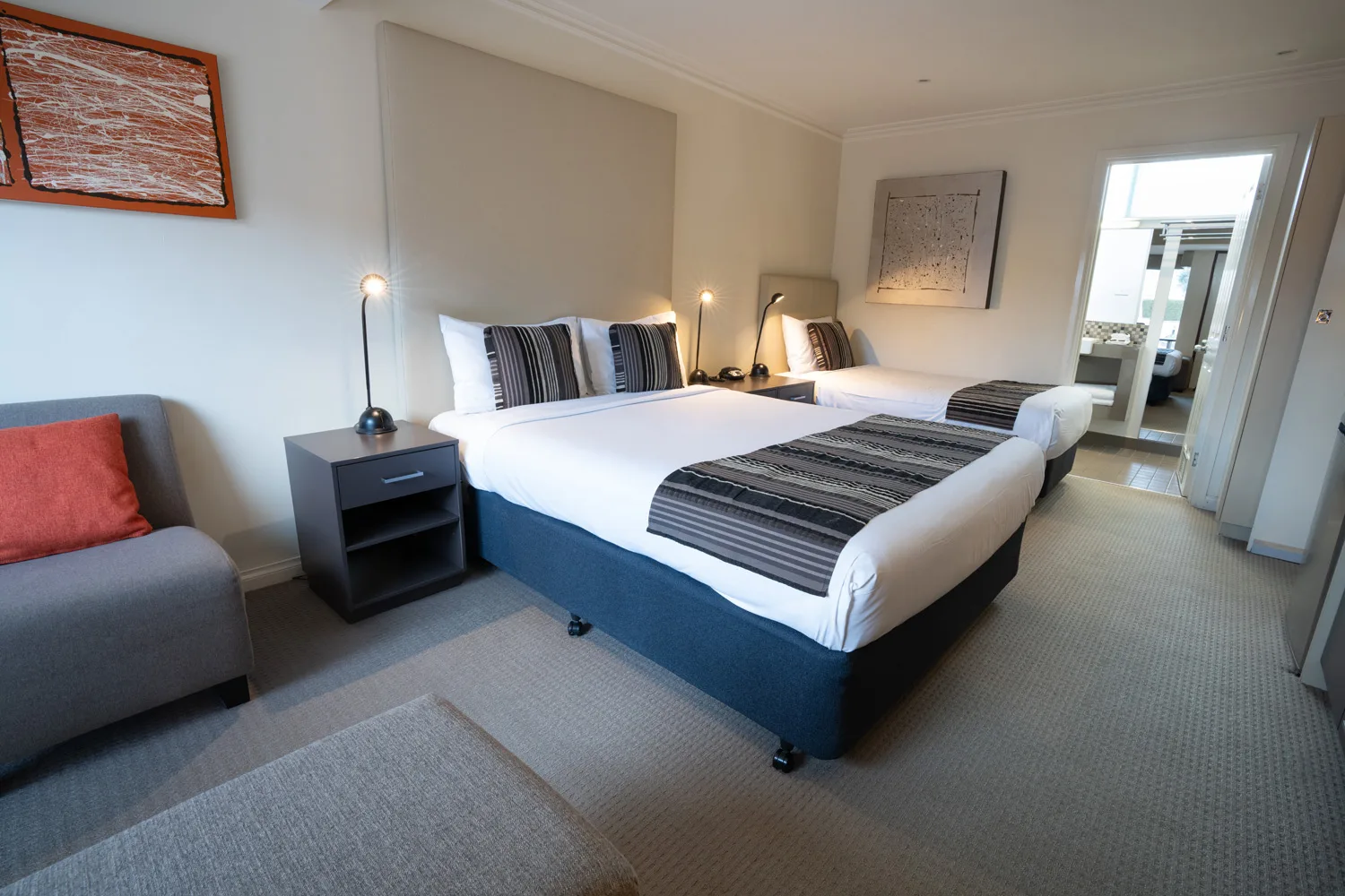 Guest room with two beds, a grey sofa and striped bed runners.