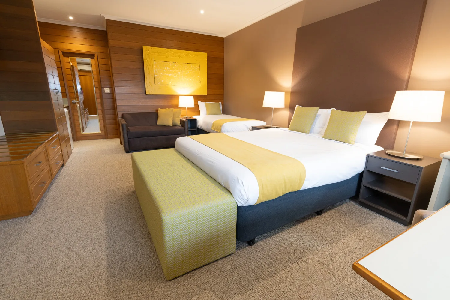 A queen bed, single bed and fold-out sofa arranged in a motel room.