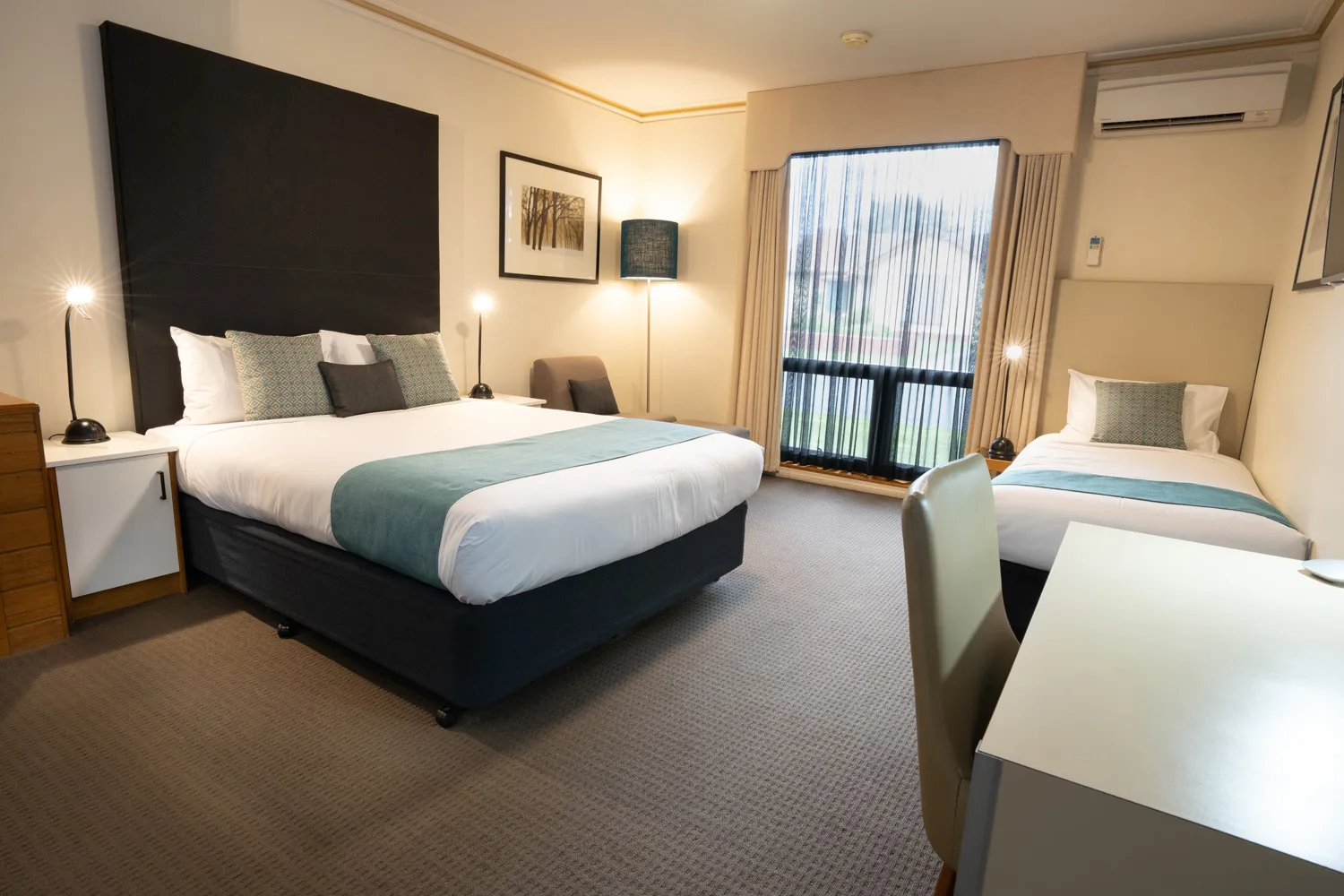 Queen bed and single bed in a room at Sovereign Park Motor Inn, with bedside lamps and natural light.