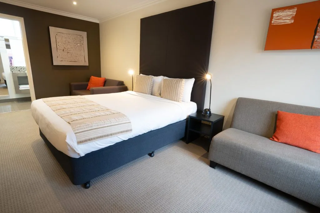 Standard unit bedroom with a large bed and grey seating accented by orange cushions.