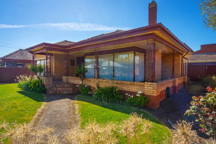 A single-storey brick house with a broad verandah sits beside a curved garden path.
