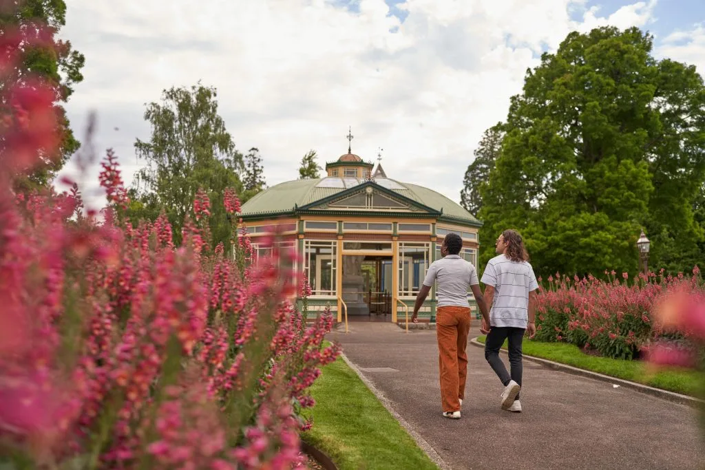 Two visitors walk towards a pavilion through flower beds at Ballarat Botanical Gardens.